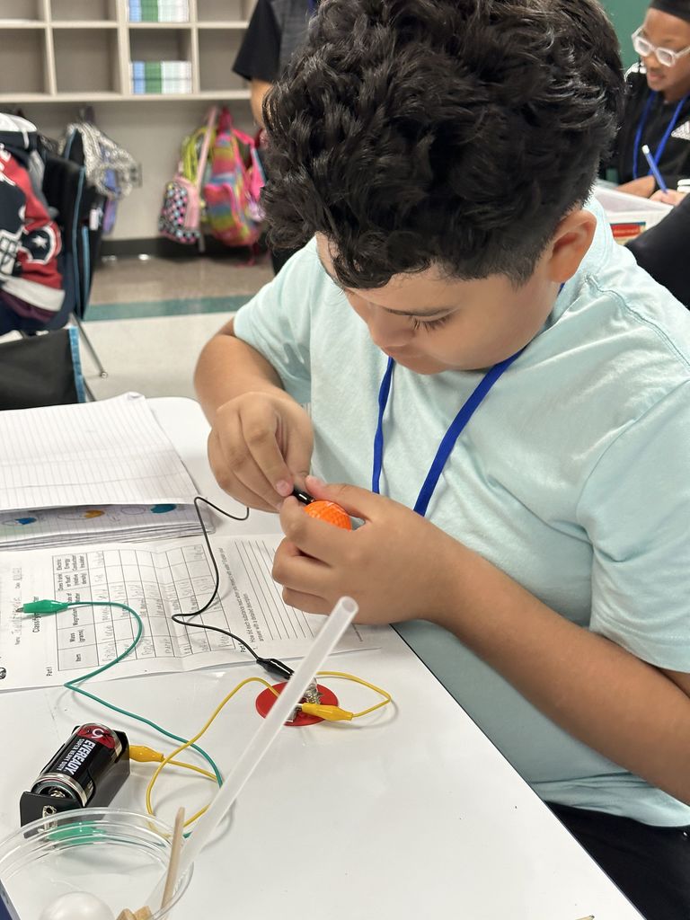 A boy tries to connect a foam golf ball to an electric circuit in a classroom.