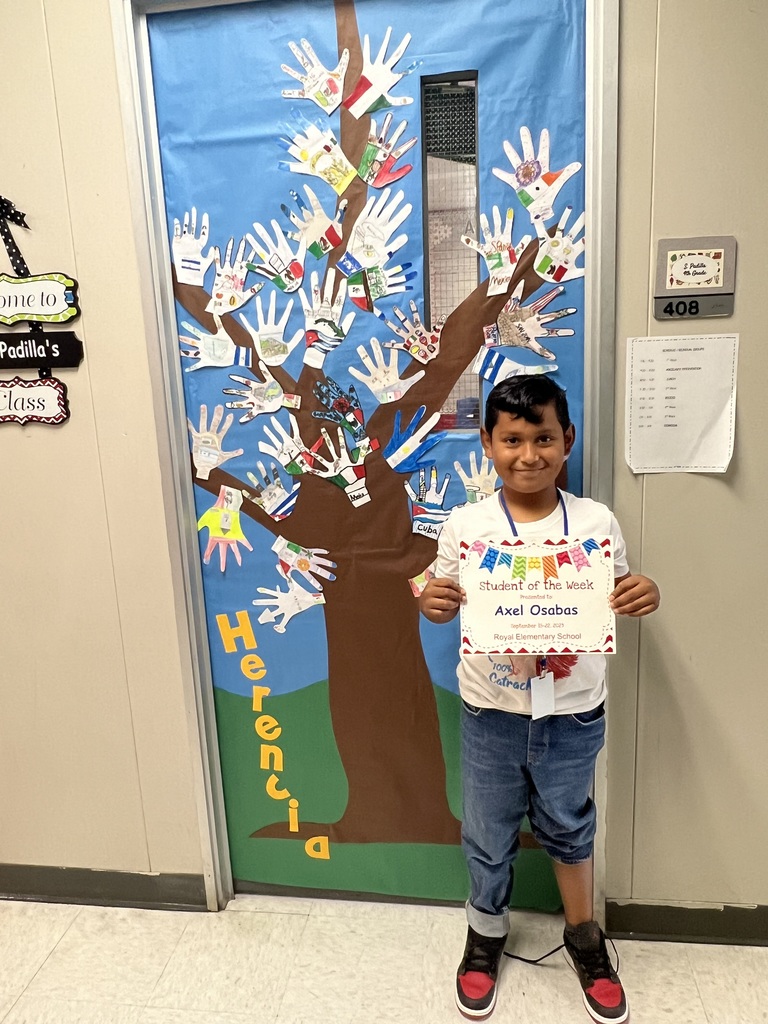 A boy stands in front of a decorated classroom door holding a paper certificate. 